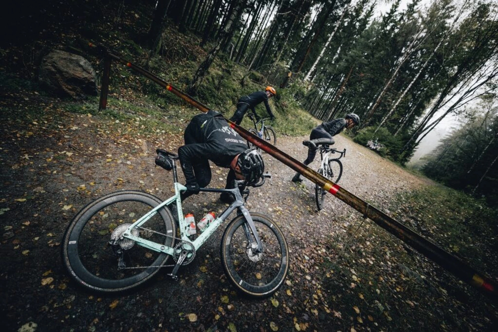 Three people cycling and ducking under a barrier