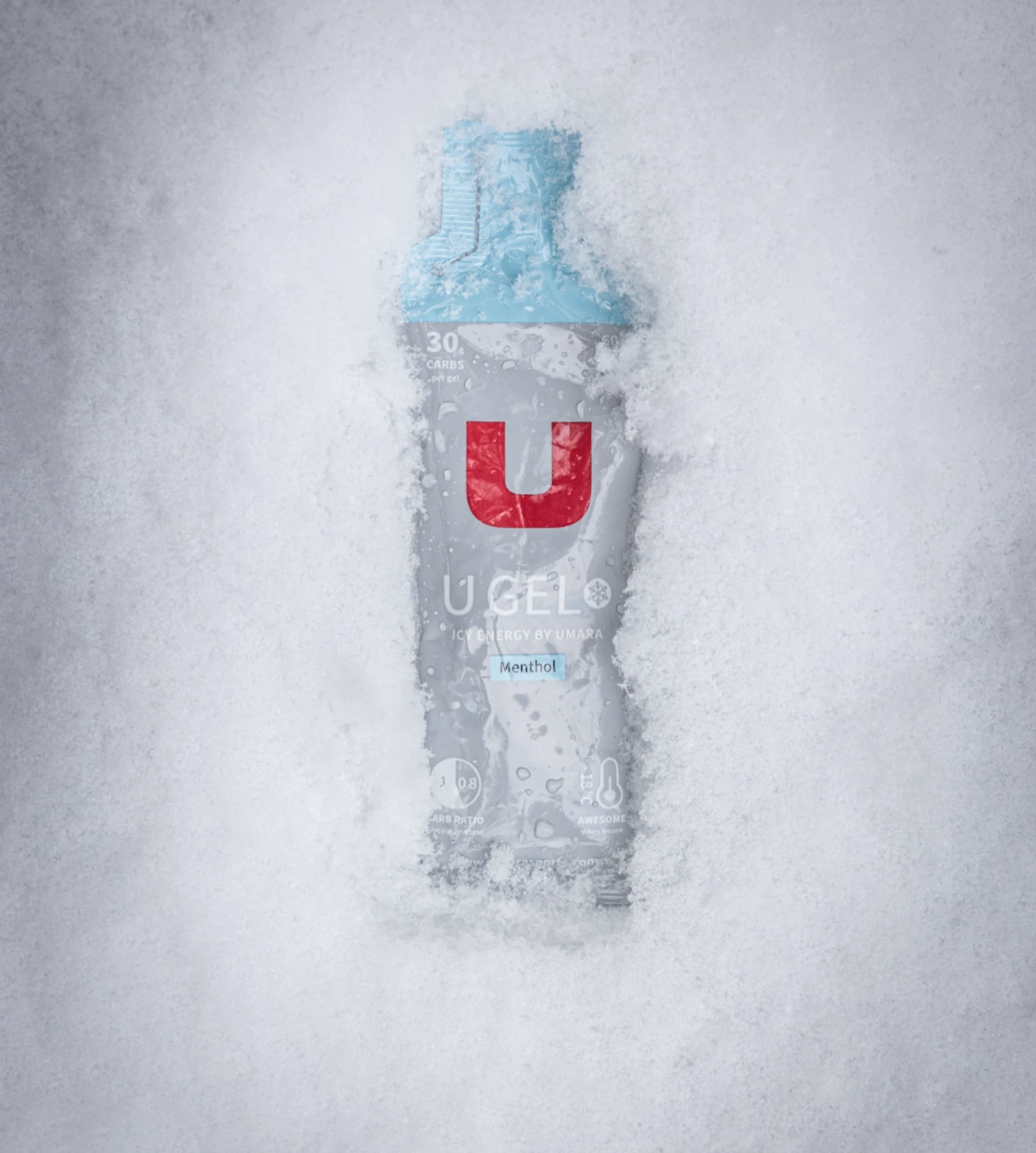 A partially snow-covered energy gel pack, featuring a distinct red "U" logo on the front.