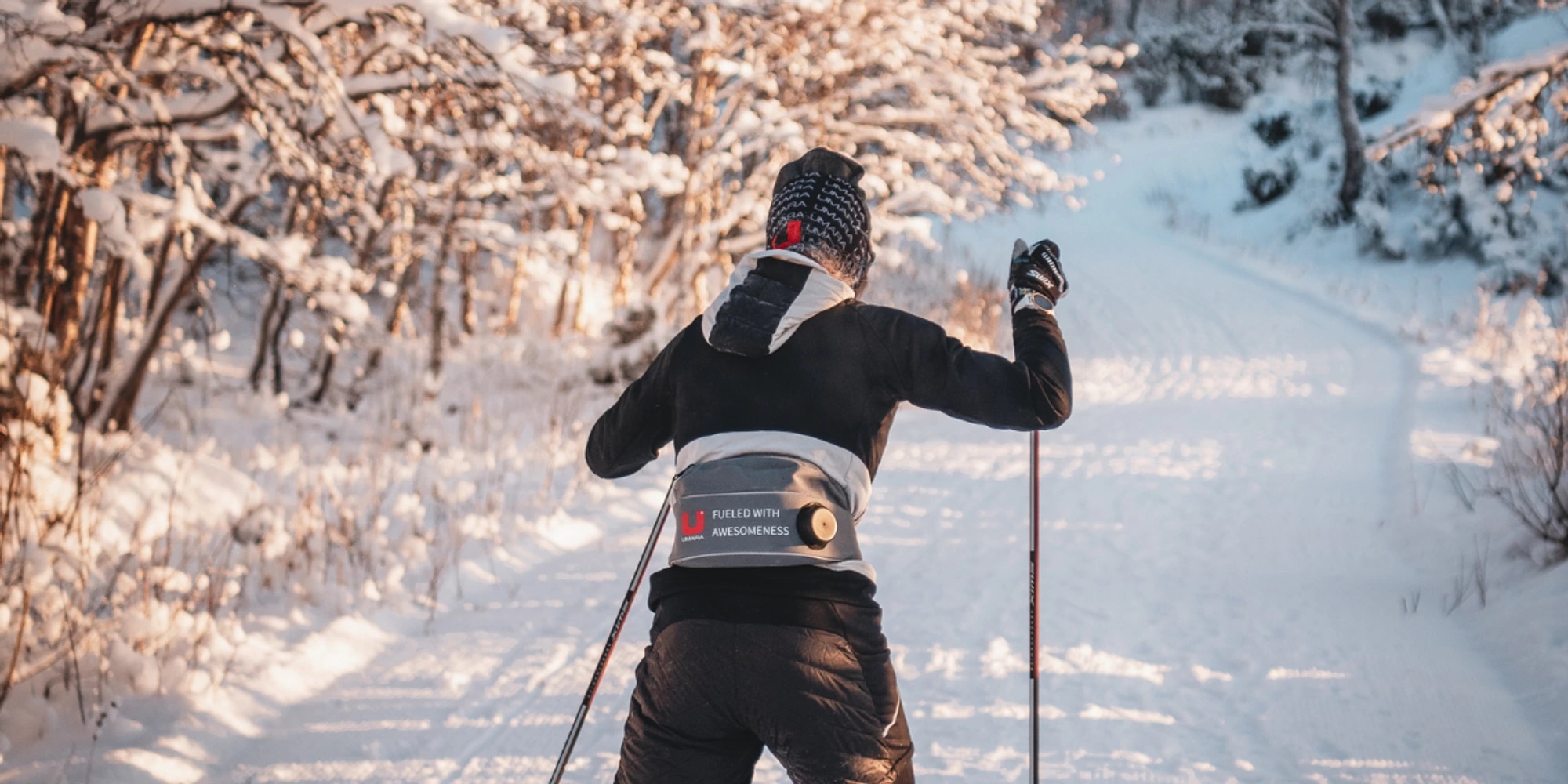 En skidåkare med umarabuff och vätskebälte. åker skidor i solsken.