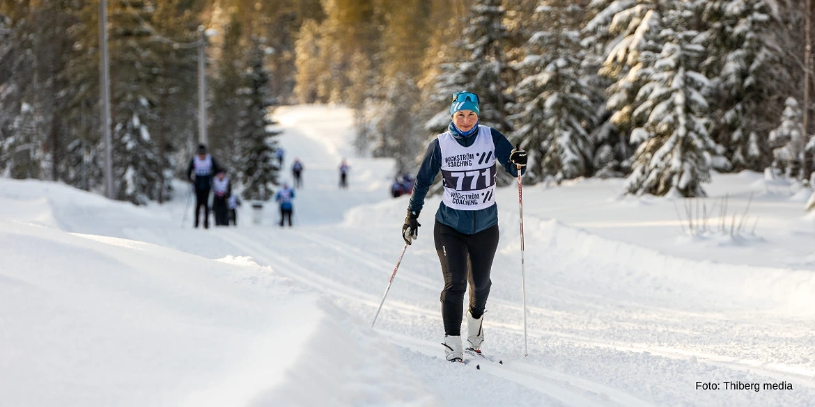 Personen åker längdskidor längs en snötäckt stig i skogen.